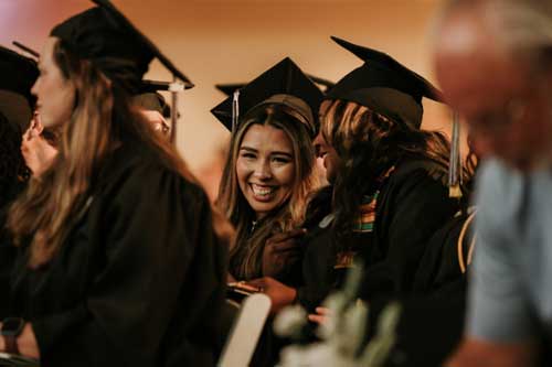 Female graduates smiling in the crowd at the spring 2024 graduation ceremony.